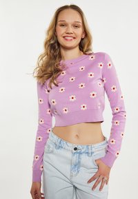 Pulover scurt violet cu flori albe și centre roșii, având manșete și hem ribbate. Purtați-l cu blugi de culoare bleu deschis, cu talie înaltă.
