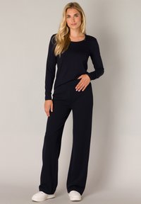 Marineblauwe longsleeve top met een ronde hals, gecombineerd met losse marineblauwe broeken. Model draagt witte sneakers en staat tegen een neutrale achtergrond.
