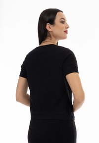 Fekete, rövid ujjú pulóver kerek nyakkivágással és bordás mandzsettával. Sima textúra, testhezálló fazon, középhosszú alj, minimalista design.