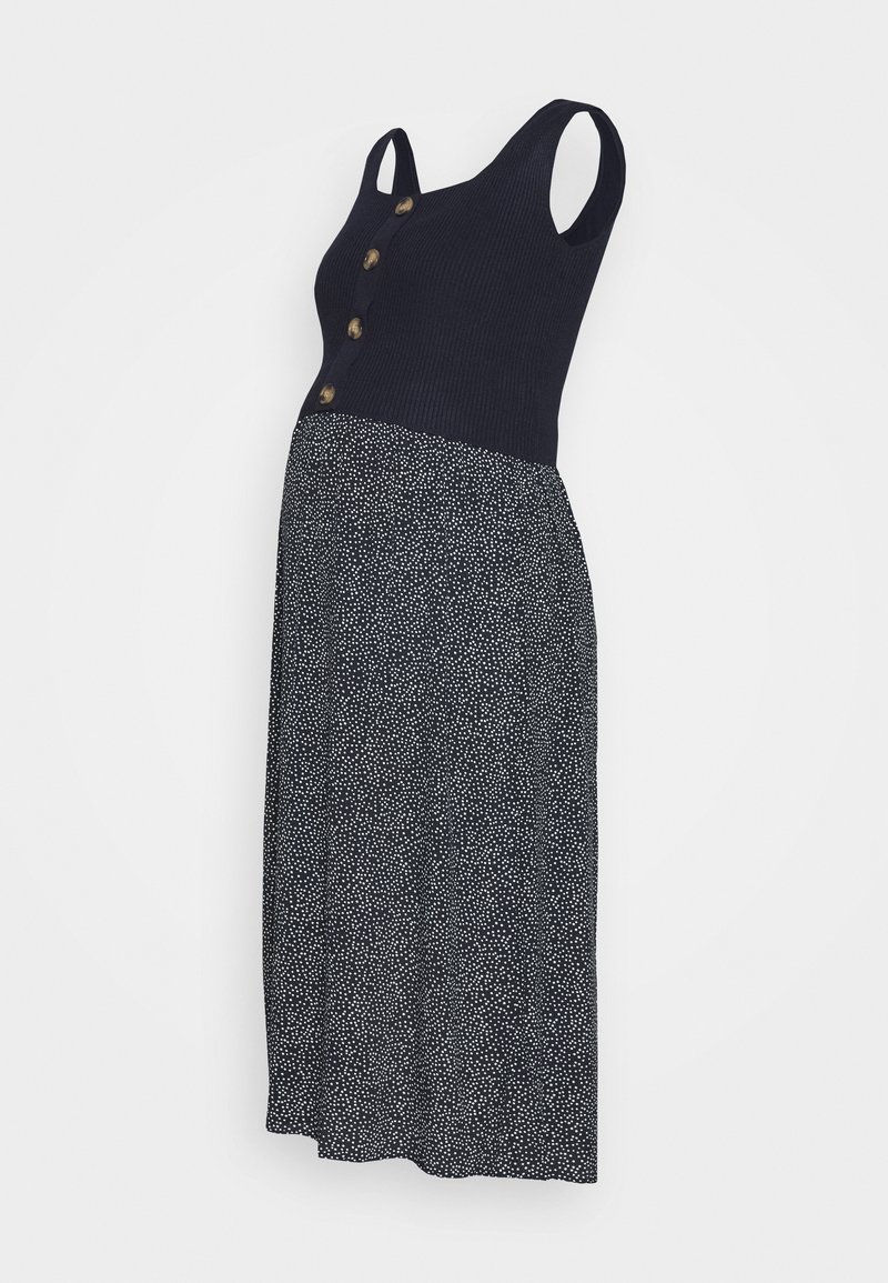 Robe de maternité sans manches avec haut côtelé noir à quatre boutons et jupe noire fluide à petits pois blancs.