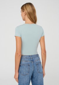 Top azzurro chiaro a maniche corte con un design aderente, lunghezza cropped e scollatura rotonda, abbinato a jeans in denim chiaro a vita alta.