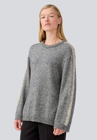 Gray knit sweater with a crew neckline, loose fit, and textured beige accents along the sleeves. Soft, warm fabric.