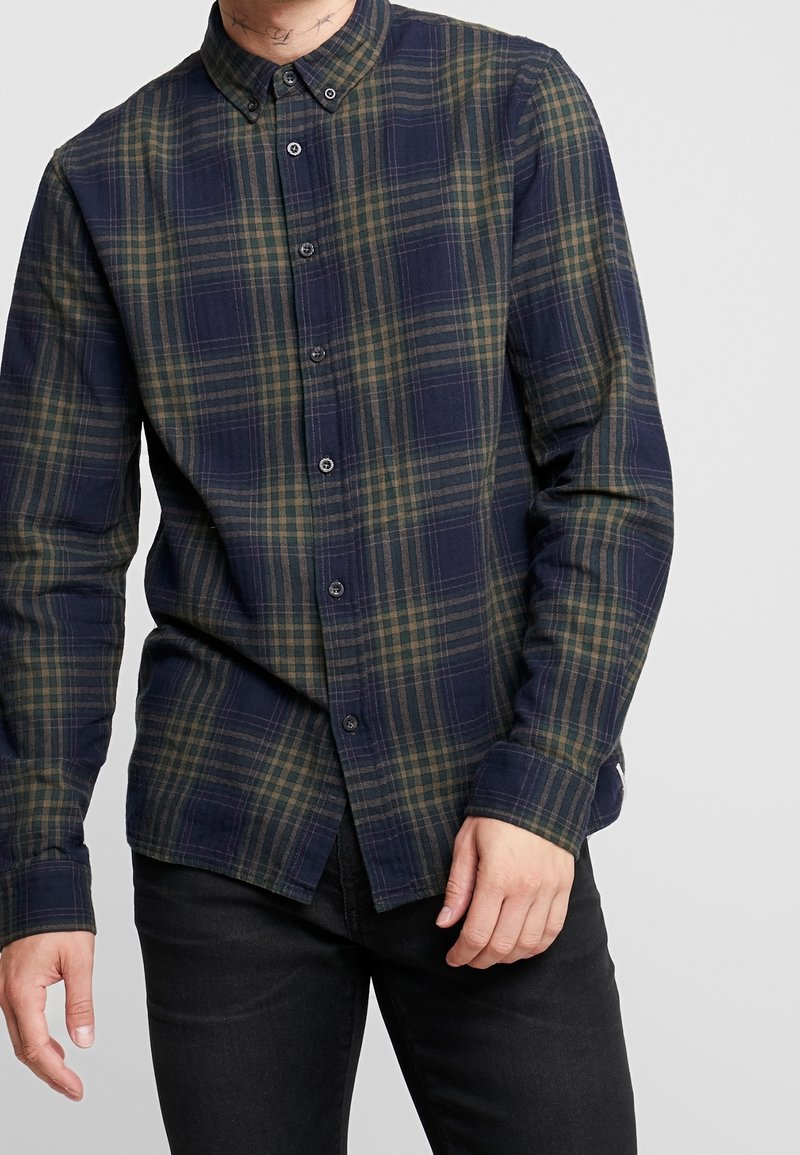Laivaston sininen ja vihreä ruudullinen pitkähihainen nappikauluspaita, jossa on etunapitus ja suora helma. Materiaali vaikuttaa pehmeältä.