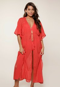 Cubierta larga de coral hecha de una tela ligera y texturizada con un patrón geométrico, de frente abierto y lazos en la cintura, con mangas anchas.