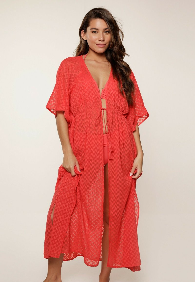 Cubierta larga de coral hecha de una tela ligera y texturizada con un patrón geométrico, de frente abierto y lazos en la cintura, con mangas anchas.