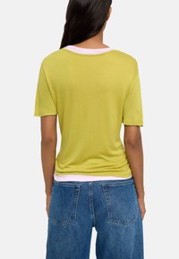 Krótki rękaw, limonkowa koszulka z okrągłym dekoltem, nałożona na różową koszulę. Połączona z luźnymi, niebieskimi dżinsami.