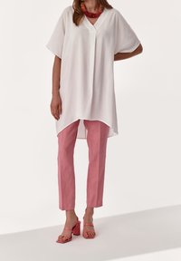 Tunika bianca ampia con scollo a V, abbinata a pantaloni di lino rosa. Accessoriata con una collana intrecciata rosa e sandali con tacco a blocco rosa.