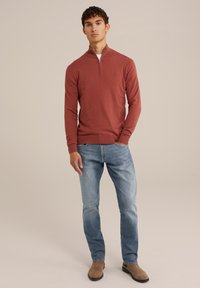 Pulover ajustat de culoare ruginiu, cu guler cu fermoar pe jumătate; asortat cu jeansi albaștri deschiși și încălțăminte bej. Design simplu, textură ușoară.