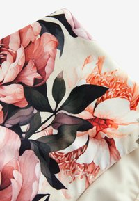 Blommigt tyg med stora rosa och orange pioner med mörkgröna blad på en krämfärgad bakgrund, slät textur och livfulla färger.