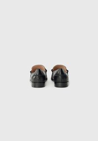 Black leather slip-on shoes with a low heel, rounded back, and minimalistic design. Smooth texture with subtle stitching details.