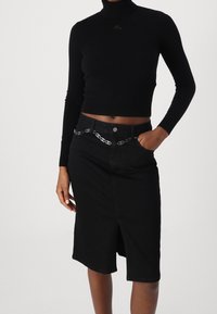 Zwarte coltrui gecombineerd met een zwarte spijkerrok met een voorkleur en een kettingriemaccent. Vlotte textuur, slim fit ontwerp.