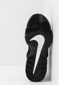 Suela de zapatilla deportiva negra con goma texturizada para agarre, que presenta un prominente diseño del logo de Nike en blanco y varios patrones de tracción.