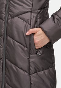 Gevoerde grijze geïsoleerde jas met een ritsvoorkant, een zijzak en een gladde, glanzende textuur met geometrische patronen.