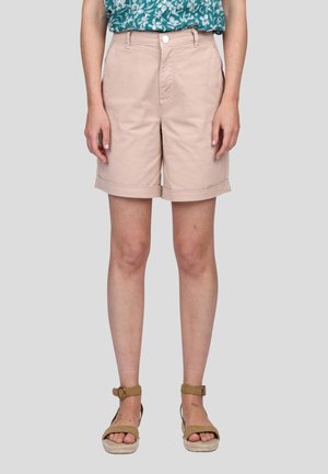 Shorts rose clair avec un ourlet retroussé, fabriqués en coton doux. Modèle portant des sandales espadrilles marron, accompagnées d'une chemise à fleurs teal.