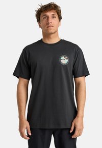 Black cotton t-shirt with short sleeves, round neckline, and a circular printed graphic on the left chest area featuring landscape elements.