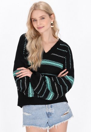 Maglione nero lavorato a maglia con motivi a zigzag turchesi e bianchi, design a scollo a V, maniche oversize, abbinato a pantaloni pantaloni in denim strappati.