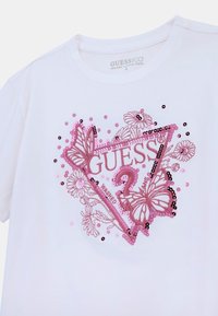 Camiseta blanca de algodón orgánico con diseño bordado en rosa que incluye lentejuelas, mariposas y motivos florales; pequeño logo en forma triangular.
