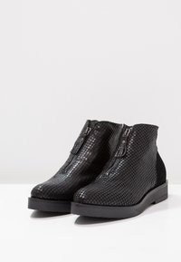 Botas de tobillo negras con un patrón de reptil texturizado en material sintético, cremalleras laterales y una suela de goma negra sólida.