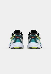 Un paio di scarpe da corsa color teal, nero, bianco e giallo neon viste da dietro su uno sfondo bianco.