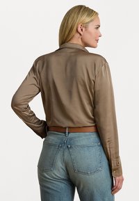 Koffiekleurige satijnen blouse met lange mouwen en een kraag, gecombineerd met lichtblauwe denim jeans met een vijf-pocket ontwerp en zichtbare stiksels.