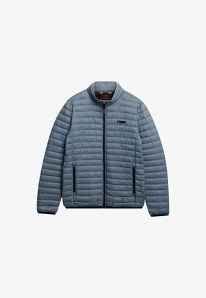 Chaqueta acolchada de color azul claro con cremallera negra y dos bolsillos con cremallera, cuello elevado y pequeño parche con logo en el pecho.
