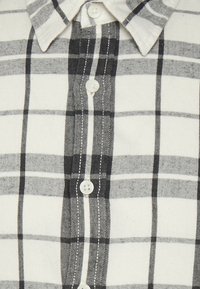 Knapp-up skjorta i svart och vitt rutig mönster, med spridd krage, vita knappar och ett mjukt, texturerat tyg.