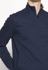 Pullover blu navy con zip a quarti realizzato in tessuto morbido, dotato di colletto, maniche lunghe e una tasca frontale con sottili dettagli di cucitura.