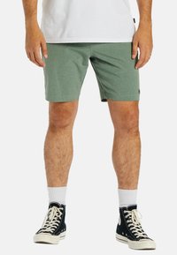 Shorts verts en tissu texturé, avec une coupe droite et des poches latérales, associés à des baskets noires et des chaussettes blanches.