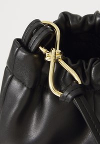 Borsa a sacchetto in pelle nera con cordoncino, dotata di un fermaglio metallico dorato e una superficie liscia, design con parte superiore arricciata e tracolla elegante.