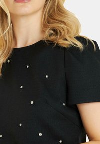 Vestido negro de manga corta con tejido texturizado, que presenta adornos de rhinestones esparcidos por el pecho y los hombros.