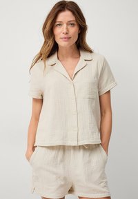 Lichtbeige loungewear set in een gestructureerde stof. Korte mouwen, knoopsluiting top met een borstzak, gecombineerd met losse shorts met elastische taille.