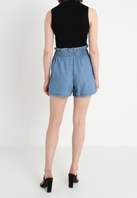Jeansshorts med mjuk textur, ljusblå färg och en resårmidja med rynkdetalj. Kombinerade med svarta sandaletter med öppen tå.