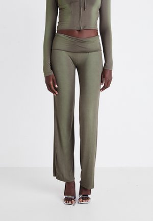 Persona che indossa pantaloni olivastro a vita alta e gamba larga e top corto a maniche lunghe coordinato con tacchi argento aperti sulle dita.