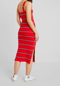 Abito midi a righe rosse con design aderente, caratterizzato da righe blu navy e bianche, spacco laterale e spalline larghe. Indossato con sneakers bianche.