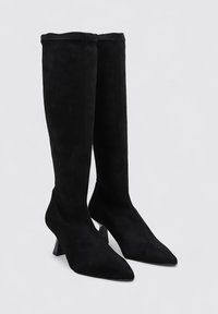 Botas altas de ante negro con punta afilada y un tacón bloque geométrico. El diseño presenta una textura suave y una silueta ajustada.