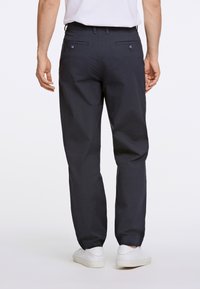 Pantaloni blu navy realizzati in un tessuto strutturato, dotati di due tasche posteriori con bottoni e una vestibilità a gamba dritta, abbinati a scarpe bianche.