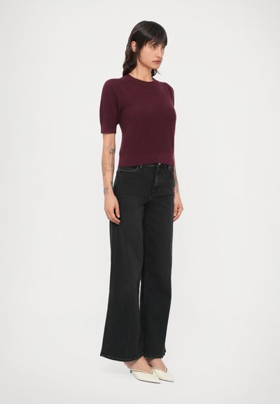 Bordó kötött felső rövid ujjakkal, magas derekú, fekete, széles szárú farmerrel és törtfehér, hegyes orrú cipővel párosítva.