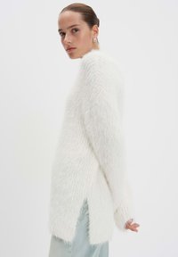 Witte, fluffy trui met een relaxed fit, voorzien van brede mouwen en zijsplitten, aangevuld met een gestructureerd patroon.