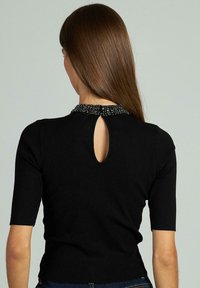Top nero a maniche corte con dettaglio a occhiello sulla schiena, caratterizzato da un colletto texturizzato con perline. Tessuto liscio e design aderente.