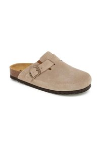 Sabots en daim beige avec un bout arrondi, une sangle réglable à boucle, une semelle en liège et une semelle en caoutchouc noir, présentant une texture lisse.
