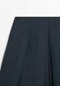 Jupe plissée gris foncé avec taille haute et détail de poche sur la couture latérale, sur fond blanc uni.