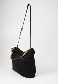 Bolso de mano de felpa negra con un exterior texturizado, cadena corta y correa de hombro de cuero. Presenta bordes redondeados y un cierre con cremallera.