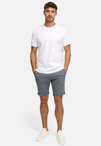 Biała koszulka z krótkim rękawem w połączeniu z szarymi spodniami w rolce i białymi sneakerami. Materiał wydaje się gładki, z klasycznym dekoltem typu crew neck.