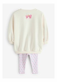 Felpa color crema chiaro con maniche a sbuffo e dettaglio con fiocco rosa sul retro, abbinata a leggings bianchi a righe con pois rosa.