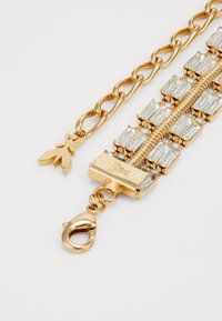 Zlati zapestnica z pravokotnimi prozornimi kristali, zasnova verige, kljuka na jermenu in dekorativni charm.
