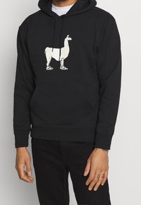 Černá mikina s kapucí s bílou grafikou lamy na přední straně, s klokánkovou kapsou a žebrovanými rukávy. Měkká tkanina s klasickým střihem.