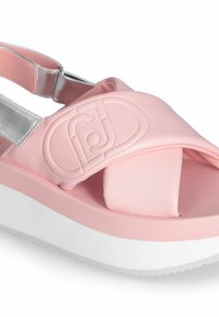 Růžové syntetické sandály s římským páskem zdobeným stříbrným akcentem, s plastickým logem a silnou bílou podrážkou. Hladký povrch po celém výrobku.