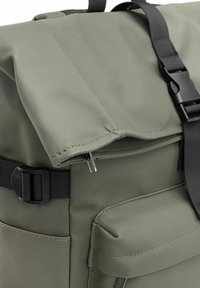 Zielony plecak z teksturowanej tkaniny, z czarnymi regulowanymi klamrami, zamykanymi przegródkami i wyściełaną przednią kieszenią.