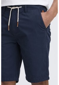 Navy blue cotton shorts with a flat front, side pockets, and a drawstring waist. Features faux leather accents and rolled hems.