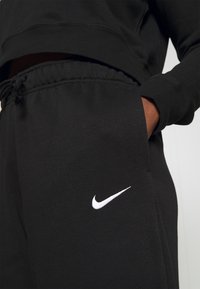 Black Nike sweatpants with elastic waistband and drawstring. Features white Nike logo on pocket. Soft fabric with a smooth texture.